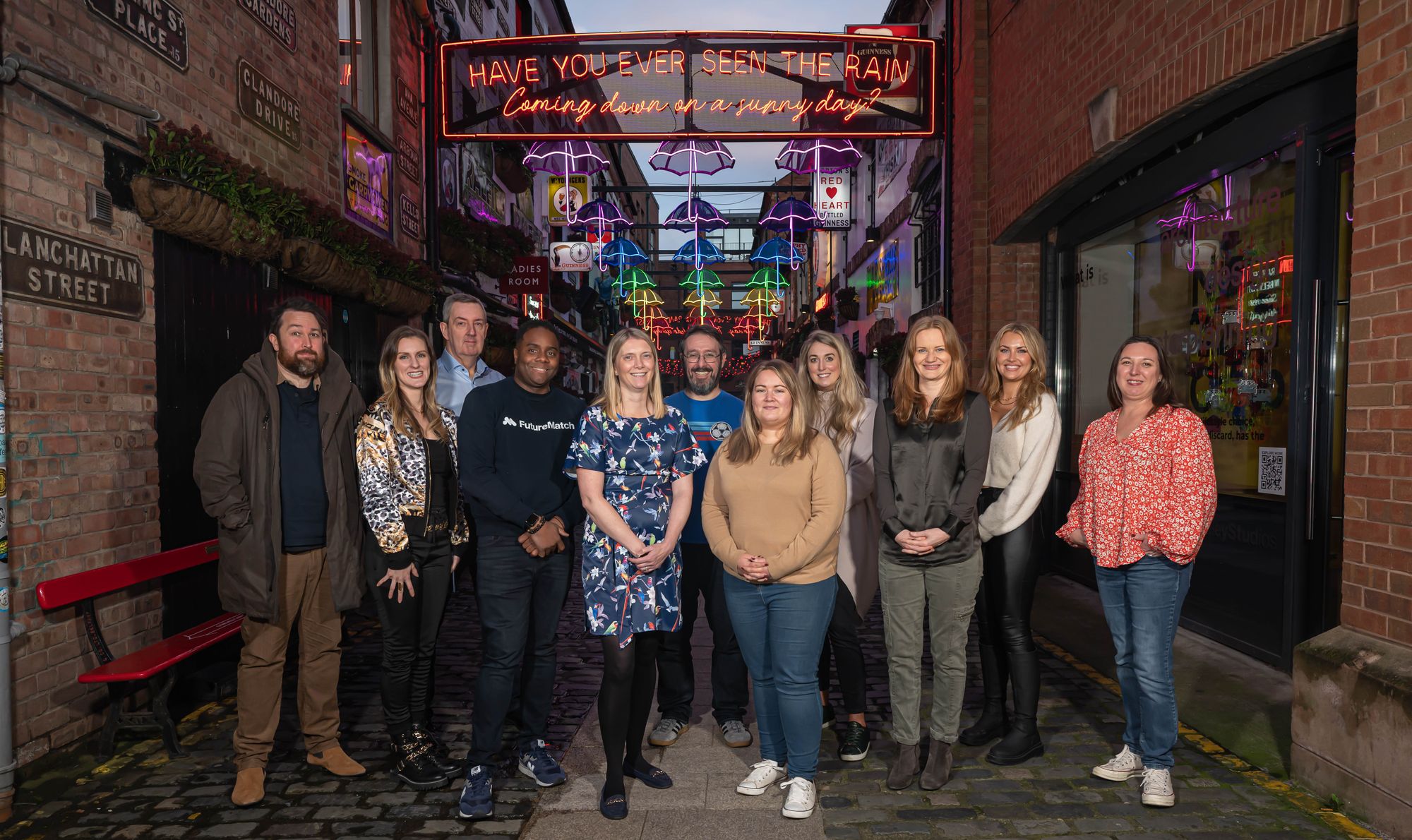 A group of individuals smiling for the camera in a decoratively lit alleyway