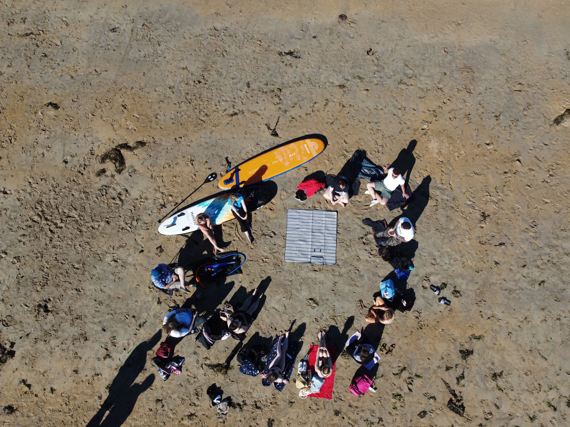 A drone photograph of a group of individuals sitting in a circle on the beach chatting