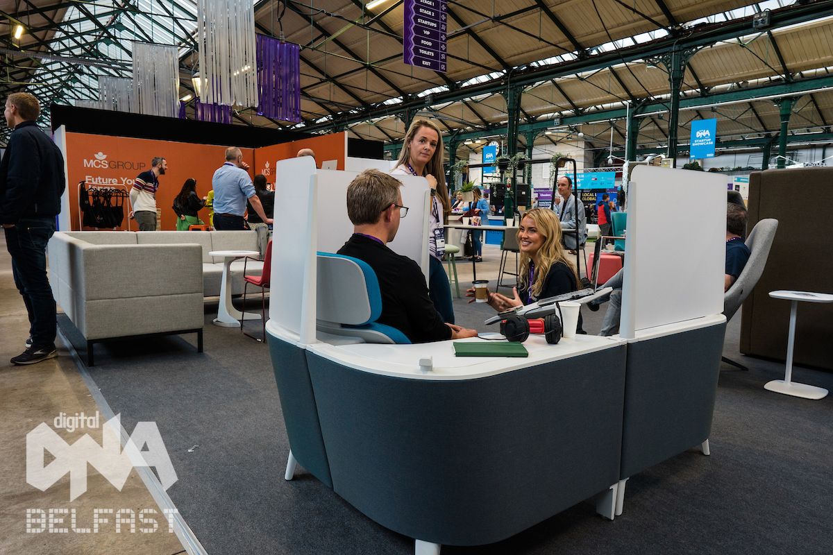 Three people are at a large tech conference chatting to each other with coffee
