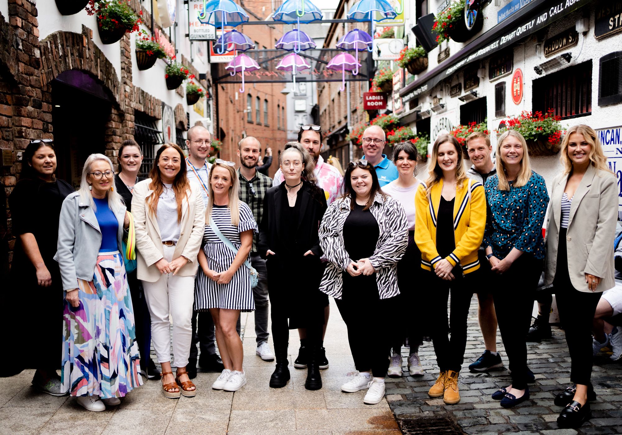 A group of around 20 people standing in a well lit alleyway during Summer
