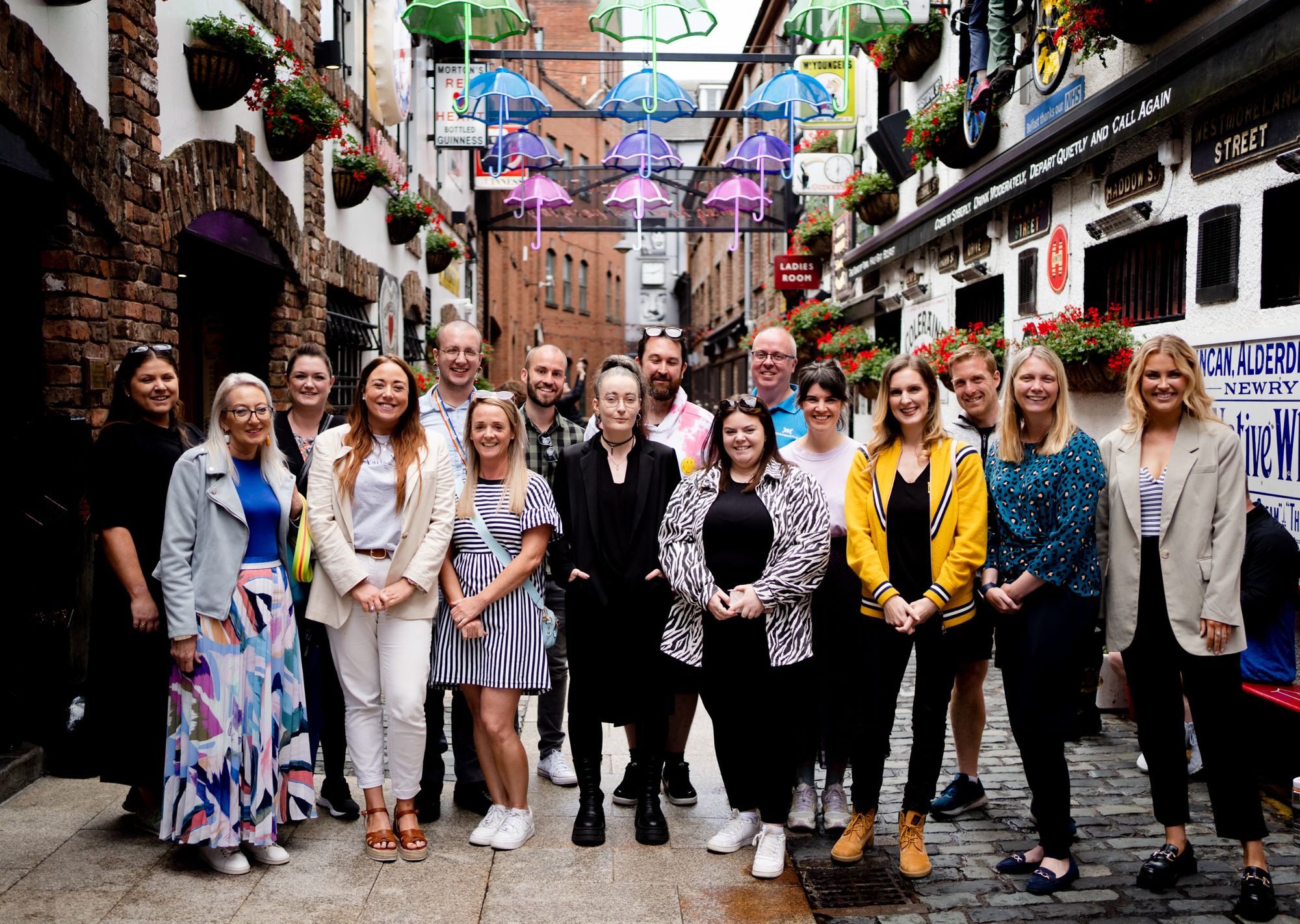 A group of individuals smiling for the camera in a decoratively lit alleyway